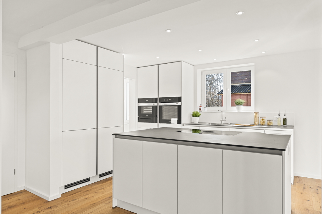 Kitchen with floor-to-ceiling cabinetry in a renovated detached house in Zürich featuring built-in oven and microwave, island with dark countertop, and oak hardwood flooring.