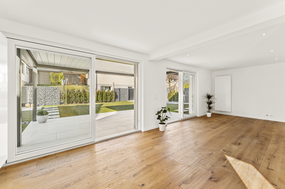 Bright living room in a renovated detached house in Zürich with floor-to-ceiling sliding glass doors opening to covered terrace and landscaped garden, oak hardwood flooring throughout.